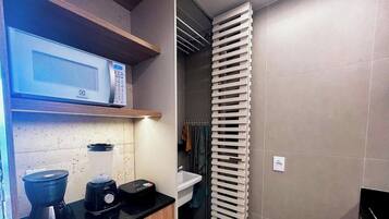 A compact kitchen with a microwave, blender, and kettle on the countertop, a white sink, and a towel rack.