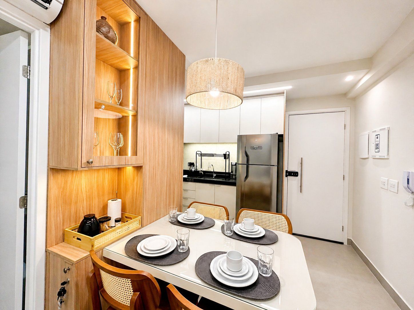 A modern kitchen with a built-in refrigerator, wooden cabinetry, and a dining area set for four with placemats and cutlery.