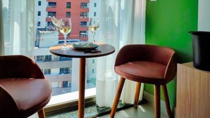 A room with a view of a building, a table with two chairs, and a green wall with decorative plates.