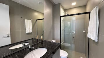 A modern bathroom with a large mirror, two sinks, a glass shower enclosure, and a white towel hanging on the wall.