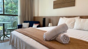 Een hotelkamer met een net opgemaakt bed, uitzicht op groen en een eethoek met een tafel en stoelen.