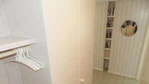 A hallway with a white door, a white shelf with a hanger, and a bookshelf with books and a decorative item. - Monique Nr. 14 Appartement/Fewo, Dusche oder Bad, WC 5-Bettwohnung by Interhome (Gstaad)