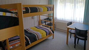 A bunk bed with striped bedding, a small table with chairs, and a window with curtains. - Monique Nr. 14 Appartement/Fewo, Dusche oder Bad, WC 5-Bettwohnung by Interhome (Gstaad)