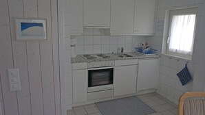A compact kitchen with white cabinets, a built-in oven, a sink, and a window with curtains. - Monique Nr. 14 Appartement/Fewo, Dusche oder Bad, WC 5-Bettwohnung by Interhome (Gstaad)