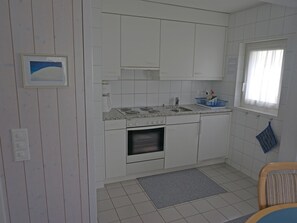 Kompakti keittiö, jossa on valkoiset kaapit, sisäänrakennettu uuni, pesuallas ja ikkuna, jossa on verhot.