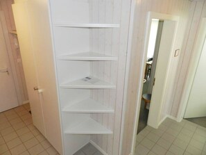 Una estanteria blanca amb tres baldas en una habitació amb panells de fusta i terra de rajola.