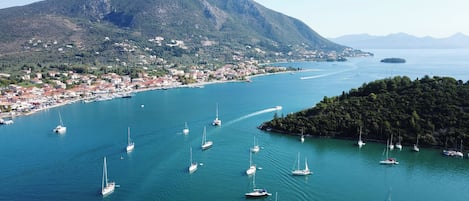 Une ville côtière dotée d’un port de plaisance où sont amarrés de nombreux voiliers, d’une petite île et d’un paysage montagneux en arrière-plan.