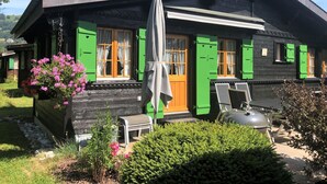 Een klassiek chalet met een schoorsteen, groene luiken en een terras met een barbecue en zitplaatsen.