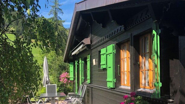 Een houten gebouw met groene luiken, een pad van stenen en een tuin vol bloemen.
