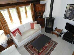 A cozy living room with a white sofa, a black table, a patterned rug, and a wood-burning stove. - Abnaki, Chalet Appartement/Fewo, Dusche oder Bad, WC 2-Bettwohnung by Interhome (Gstaad)