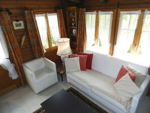 Ein gemütliches Zimmer mit einem weißen Sofa, einem kleinen weißen Sessel und einer Lampe.