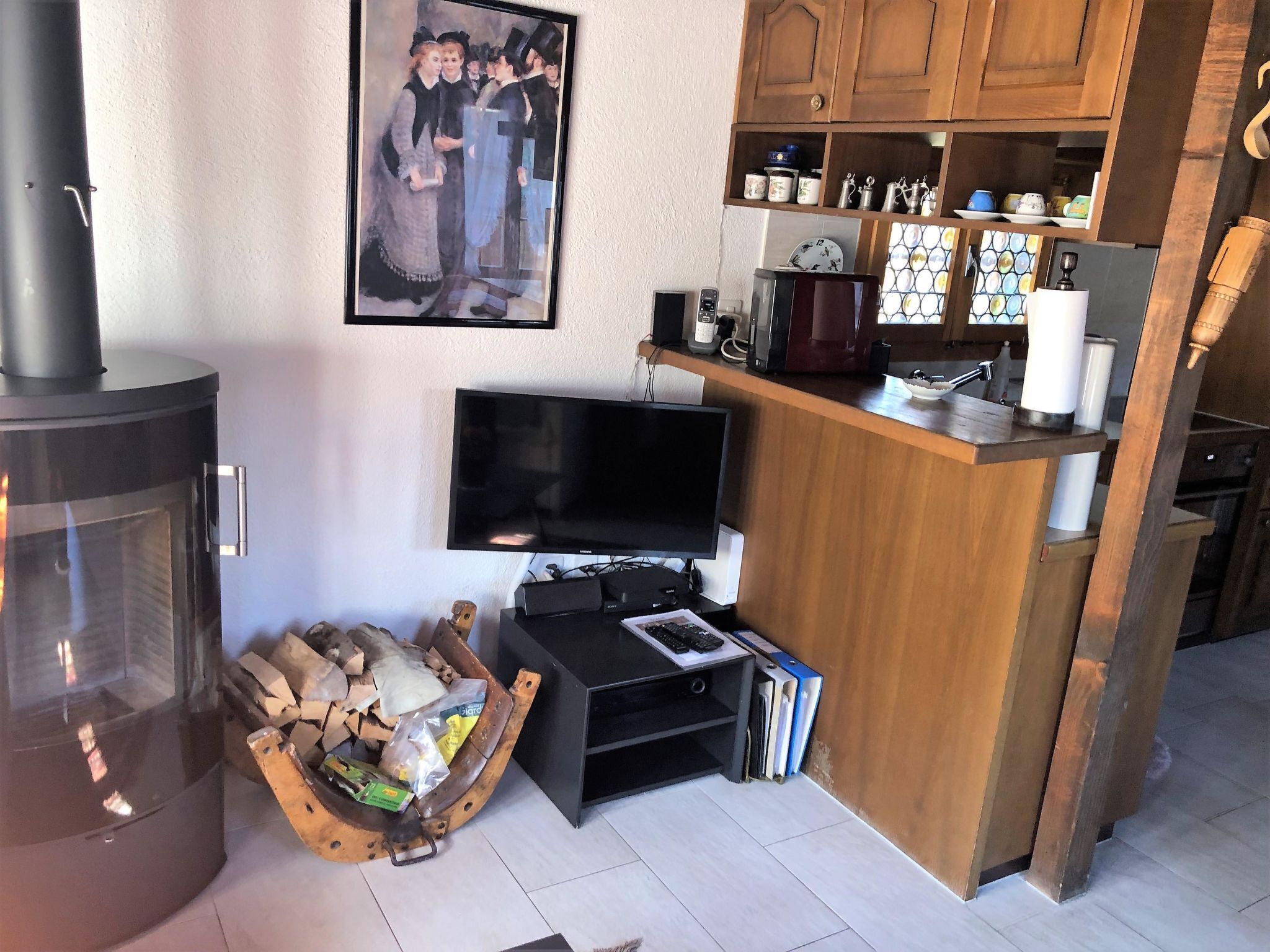 Olohuone, jossa on takka, televisio, pieni keittiöalue puukehikoilla ja seinällä kehystetty taulu.