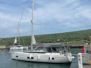 A marina with a white sailboat docked, a covered area, and a hill with greenery in the background.