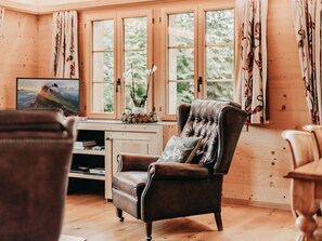 A cozy room with a leather armchair, a wooden desk, and a large window with curtains. - Giferblick Appartement/Fewo, Dusche und Bad, WC 6-Bettwohnung by Interhome (Gstaad)