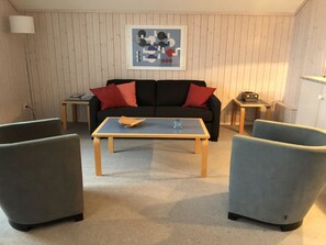 A living room with a sofa, two armchairs, a coffee table, a framed abstract art piece, a radio, and a lamp. - Monique Nr. 1 Appartement/Fewo, Dusche oder Bad, WC 4-Bettwohnung by Interhome (Gstaad)