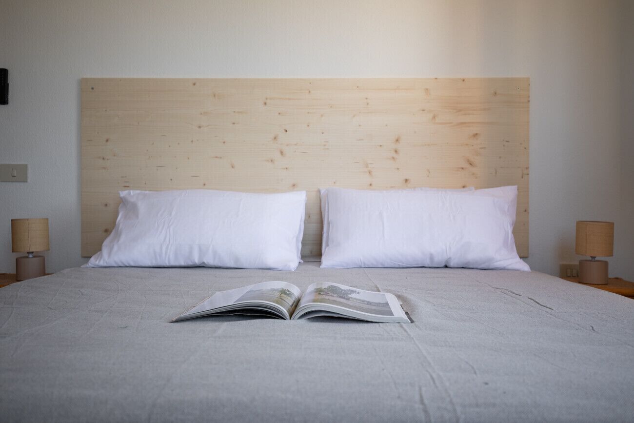 Ein Bett mit Holz-Kopfteil, zwei weiße Kissen und eine offene Zeitschrift darauf.