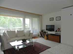 A modern living room with a sofa, coffee table, TV, and a bookshelf. - La Sarine 124 Appartement/Fewo, Dusche oder Bad, WC 4-Bettwohnung by Interhome (Gstaad)