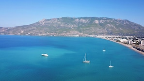A coastal town with clear blue waters, a mountain in the background, and several boats.