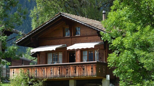 Una baita di legno con un balcone, immersa tra gli alberi.