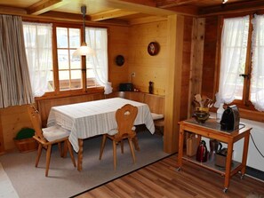 A cozy cabin-style room with a wooden interior, a dining table with chairs, a small kitchen area with a coffee maker, and a window with curtains. - Marmotte, Chalet Appartement/Fewo, Dusche, WC 4-Bettwohnung by Interhome (Lauenen b. Gstaad)