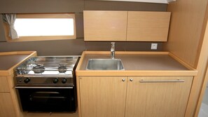 A compact kitchenette with a stove, oven, sink, and wooden cabinets. - Sun-Kissed Sailing Adventure in Istria, Croatia (Pula)