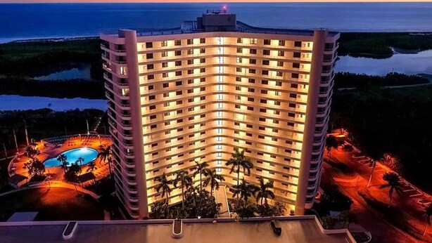 Ett högt hotell med en pool, omgivet av grönska och med utsikt över havet.