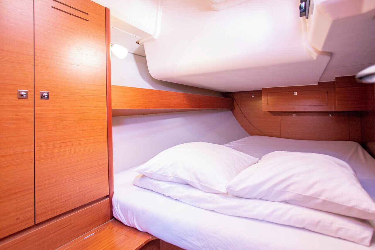 A compact, well-lit cabin with a bed, wooden cabinetry, and a ceiling light.