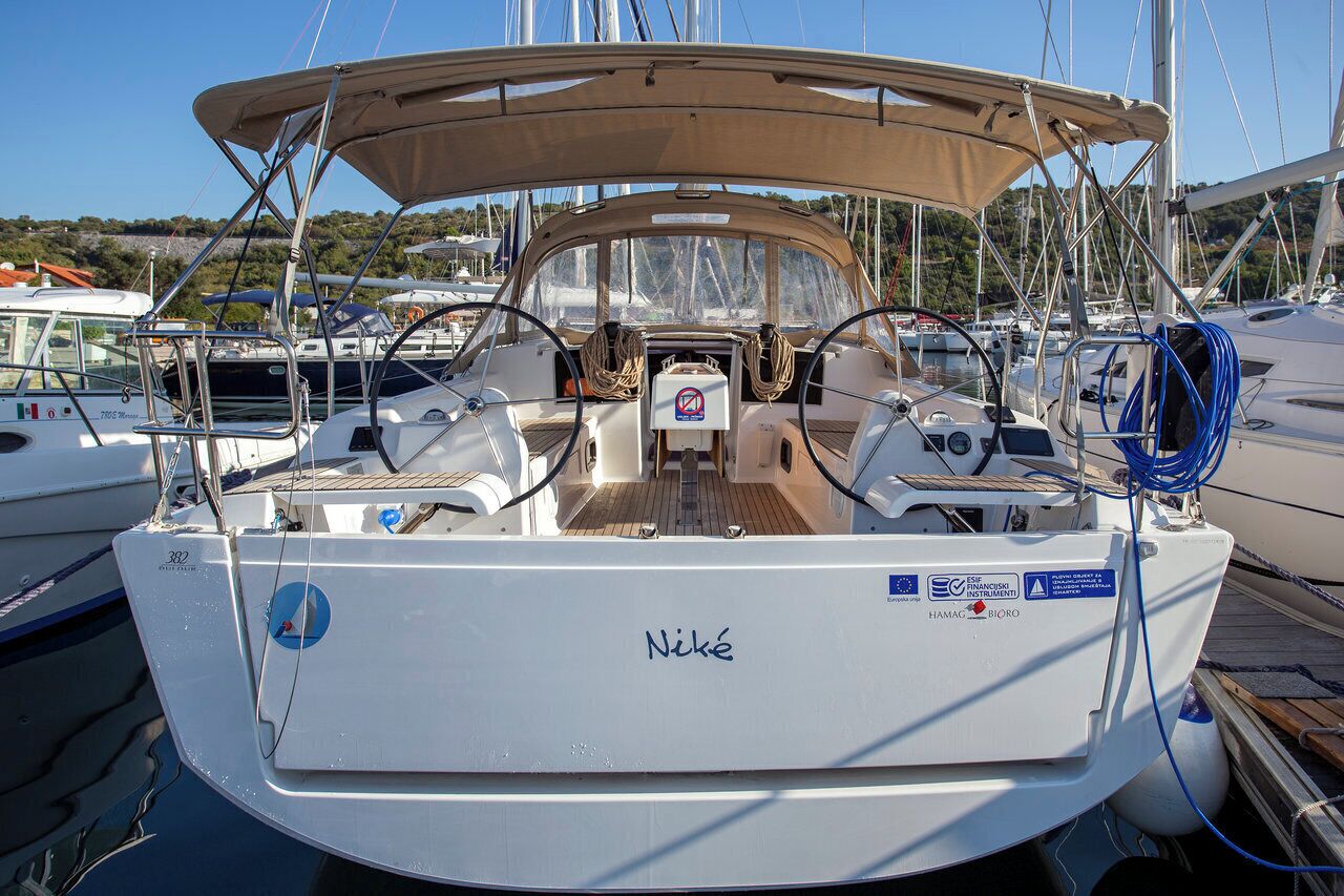 A sailboat named 'Niké' docked at a marina with a covered cockpit, steering wheel, and various navigational instruments.