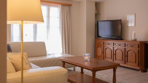 A living room with a sofa, a coffee table, a television on a wooden cabinet, and a lamp. - Fichte (Marija) Appartement/Fewo, Dusche und Bad, WC, 2 Schlafräume by Interhome (Gstaad)