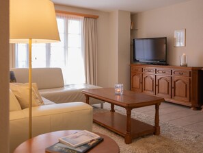 A living room with a sofa, a coffee table, a television on a wooden cabinet, and a lamp. - Fichte (Marija) Appartement/Fewo, Dusche und Bad, WC, 2 Schlafräume by Interhome (Gstaad)