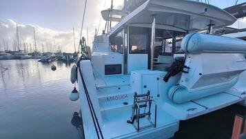 Un yacht blanc nommé MAGLICA était amarré dans une marina, à côté d’autres bateaux. On pouvait y voir une échelle et un treuil sur le pont.