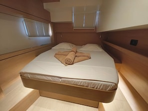 A neatly made bed with a rolled towel, wooden headboard, and a window with blinds.