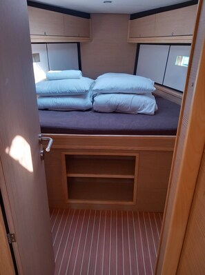 A compact bed with pillows and a headboard, wooden cabinetry above, and a striped floor. - Sun-Kissed Sailing Adventure in Zadar, Croatia (Biograd na moru)