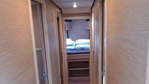 Um corredor estreito com paredes de painel de madeira e chão listrado, levando a um quarto com cama e janela.