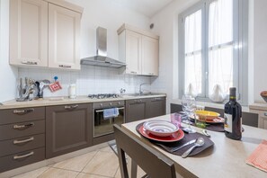 Eine moderne Küche mit Herd, Backofen und Spüle. Ein Esstisch mit Tellern und einer Weinflasche steht daneben.