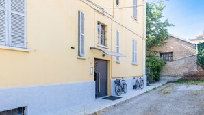 A yellow building with a door, windows, and a bicycle parked outside. - GuestHost - Bright and Cozy Apartment with Parking (Parma)
