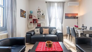 A modern living room with a black sofa, a red patterned rug, and a dining area with a table and chairs. - GuestHost - Bright and Cozy Apartment with Parking (Parma)