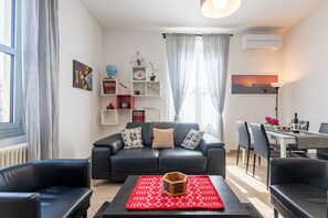Ein modernes Wohnzimmer mit einem schwarzen Sofa, einem roten Teppich mit Muster und einem Essbereich mit Tisch und Stühlen.