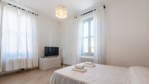 A bedroom with a bed, a TV, a radiator, and curtains. - GuestHost - Bright and Cozy Apartment with Parking (Parma)