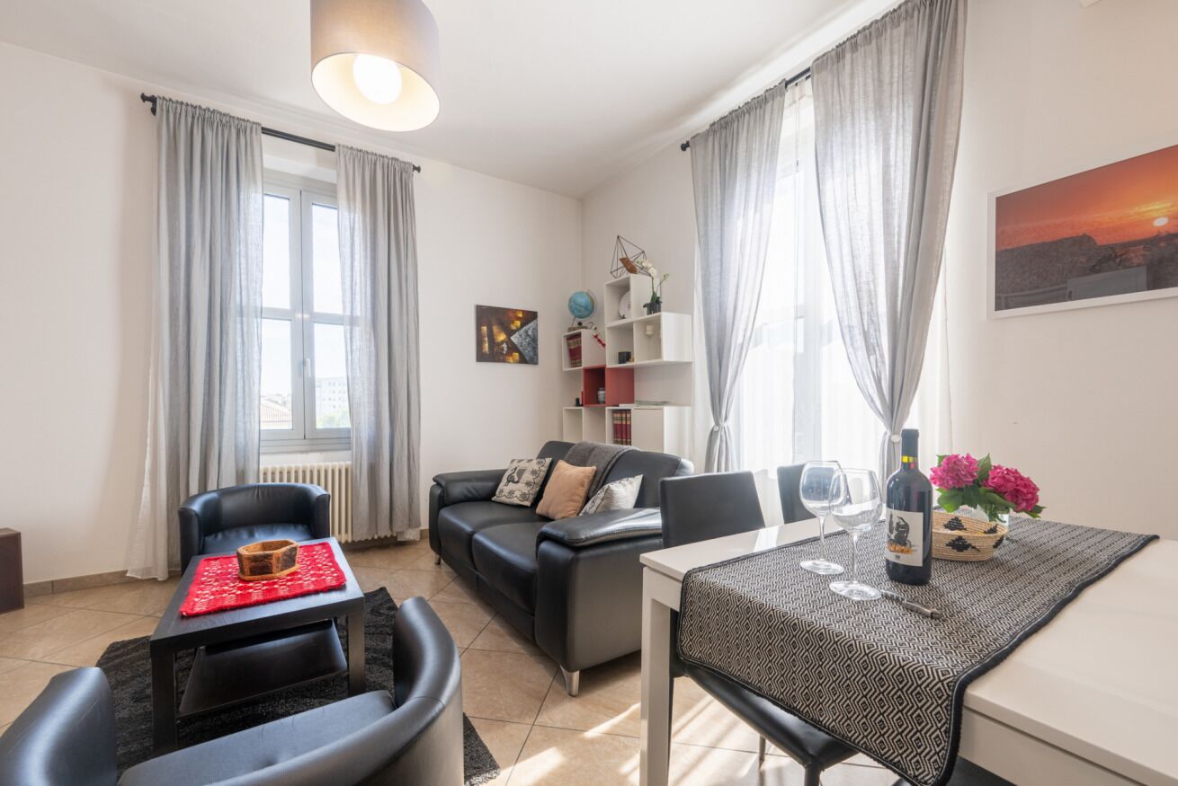 A modern living room with a sofa, a dining table with chairs, a red table runner, a globe, and a wine bottle on the table.