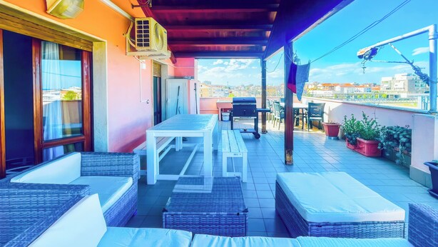 Terraço no telhado com móveis de vime, uma mesa e plantas em vasos.