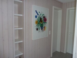 A room with a white door, a white wall with a colorful abstract painting, and a white shelving unit. - Suzanne Nr. 18 Appartement/Fewo, Dusche oder Bad, WC 5-Bettwohnung by Interhome (Gstaad)