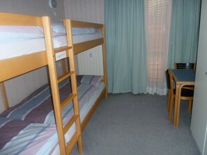 Een slaapkamer met een stapelbed, bureau en stoel, een raam met gordijnen, en een radiator.
