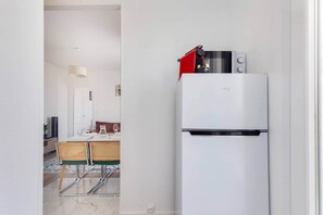 A compact kitchen with a white refrigerator, a red appliance on top, and a dining area with a table and chairs. - Paris Chic · Percy · Issy RER · Exhibition Center (Clamart)