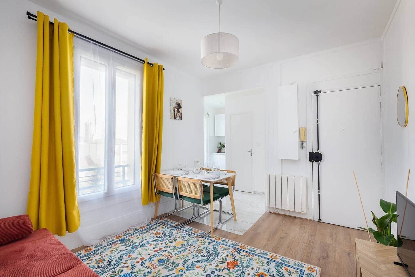 A bright room with a dining table, yellow curtains, a radiator, and a plant.