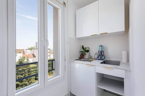 Eine kleine Küche mit weißen Schränken, einem Fenster und einem Balkon.