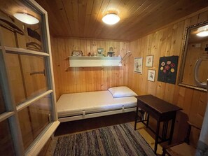 A small, compact room with wooden walls, a single bed, a small table, and a shelf with various items. - Obegghuus Appartement/Fewo, Dusche oder Bad, WC 7-Bettwohnung by Interhome (Zweisimmen)