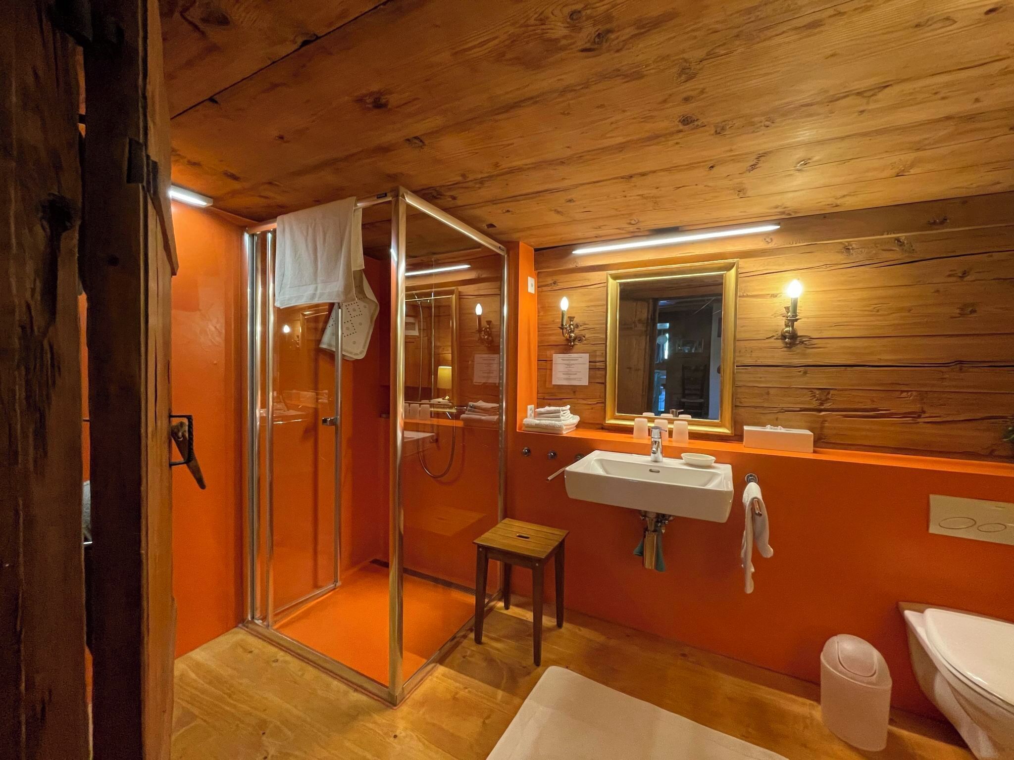 Bany d'una cabana de fusta amb una dutxa de vidre, un lavabo i un vàter.
