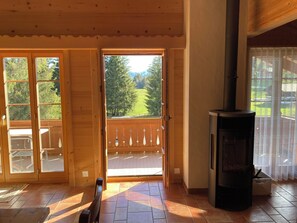 A wooden interior with a fireplace, a sliding glass door leading to a balcony, and a view of a green landscape. - Fichte (Sulliger) Appartement/Fewo, Dusche oder Bad, WC 6-Bettwohnung by Interhome (Gstaad)