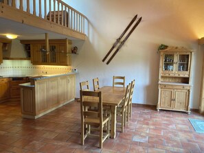 A kitchen with wooden cabinets, a dining table with chairs, a staircase, and a cabinet with glass doors. - Fichte (Sulliger) Appartement/Fewo, Dusche oder Bad, WC 6-Bettwohnung by Interhome (Gstaad)